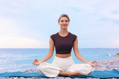 Photo of Young woman practicing yoga on mat at beach