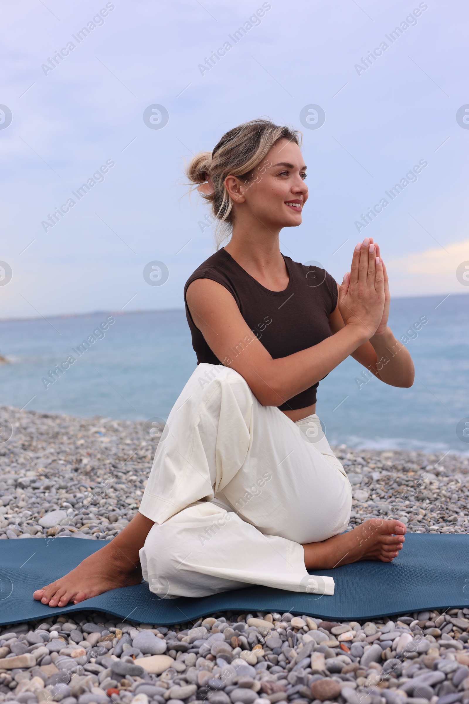 Photo of Young woman practicing yoga on mat at beach