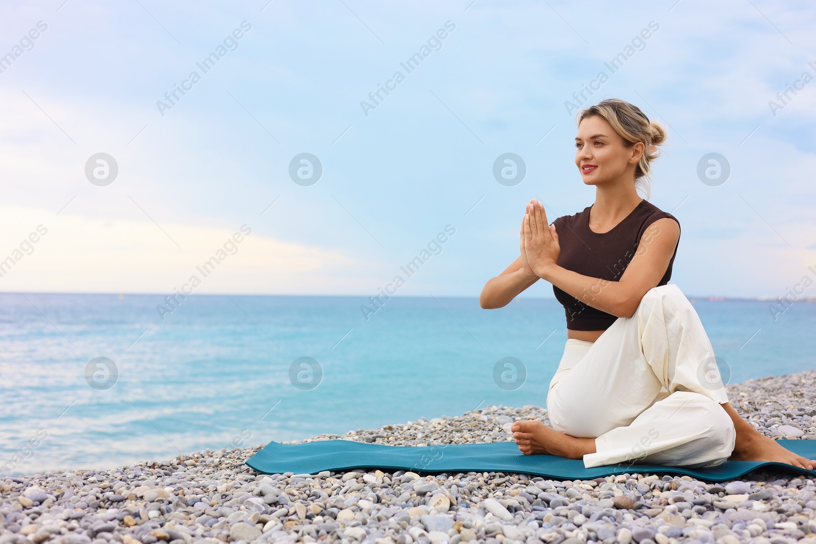 Photo of Young woman practicing yoga on mat at beach, space for text