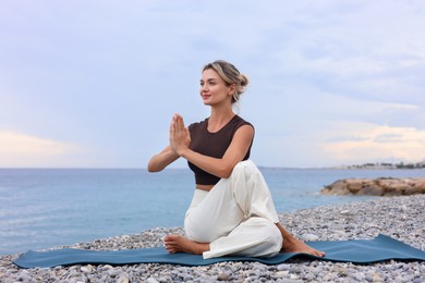 Photo of Young woman practicing yoga on mat at beach