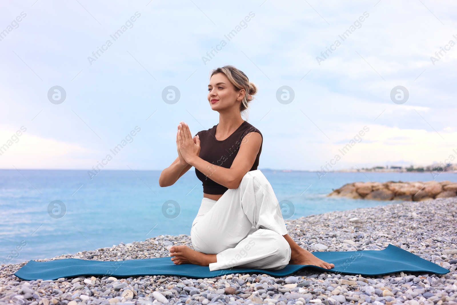 Photo of Young woman practicing yoga on mat at beach