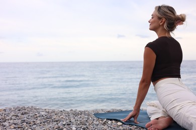 Photo of Young woman practicing yoga on mat at beach. Space for text