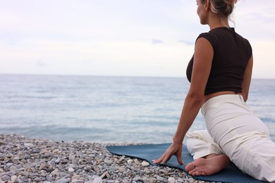 Photo of Young woman practicing yoga on mat at beach. Space for text