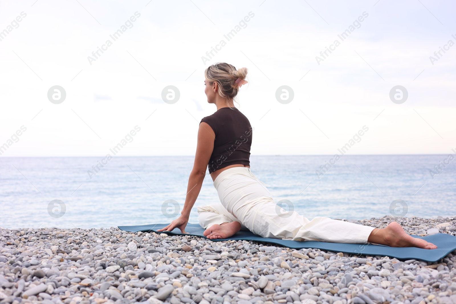 Photo of Young woman practicing yoga on mat at beach