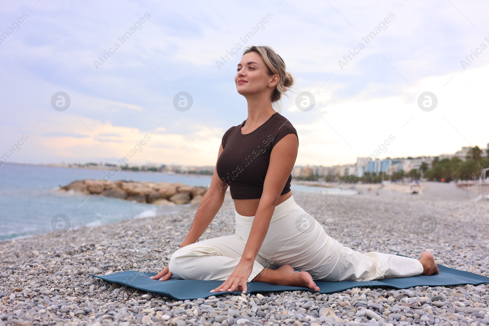 Photo of Young woman practicing yoga on mat at beach