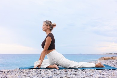 Photo of Young woman practicing yoga on mat at beach