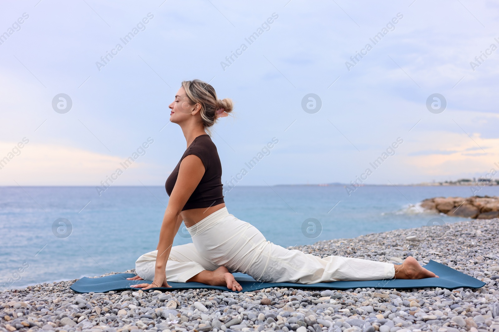 Photo of Young woman practicing yoga on mat at beach
