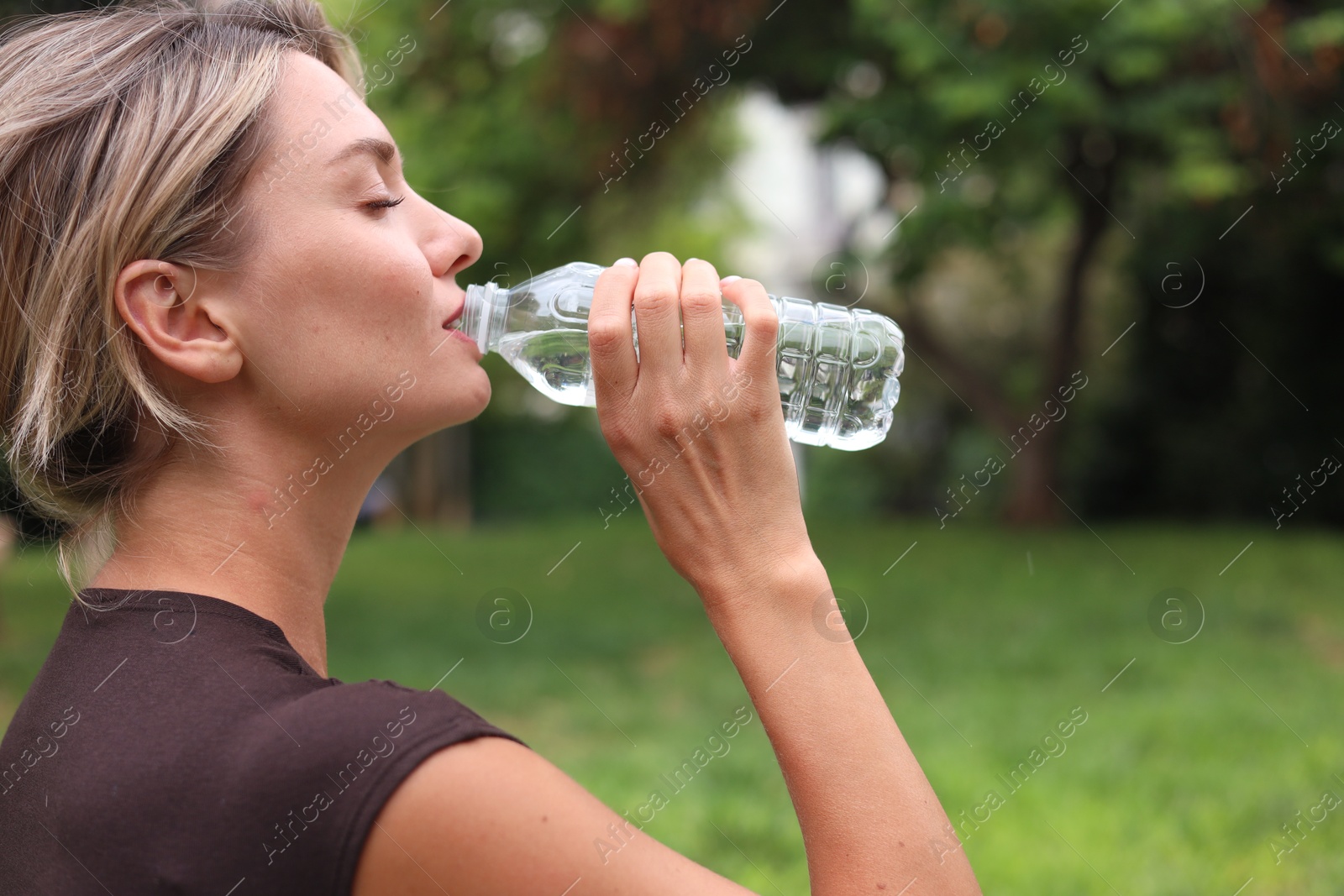 Photo of Young woman drinking water in park, space for text