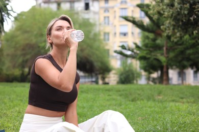 Photo of Young woman drinking water on yoga mat in park