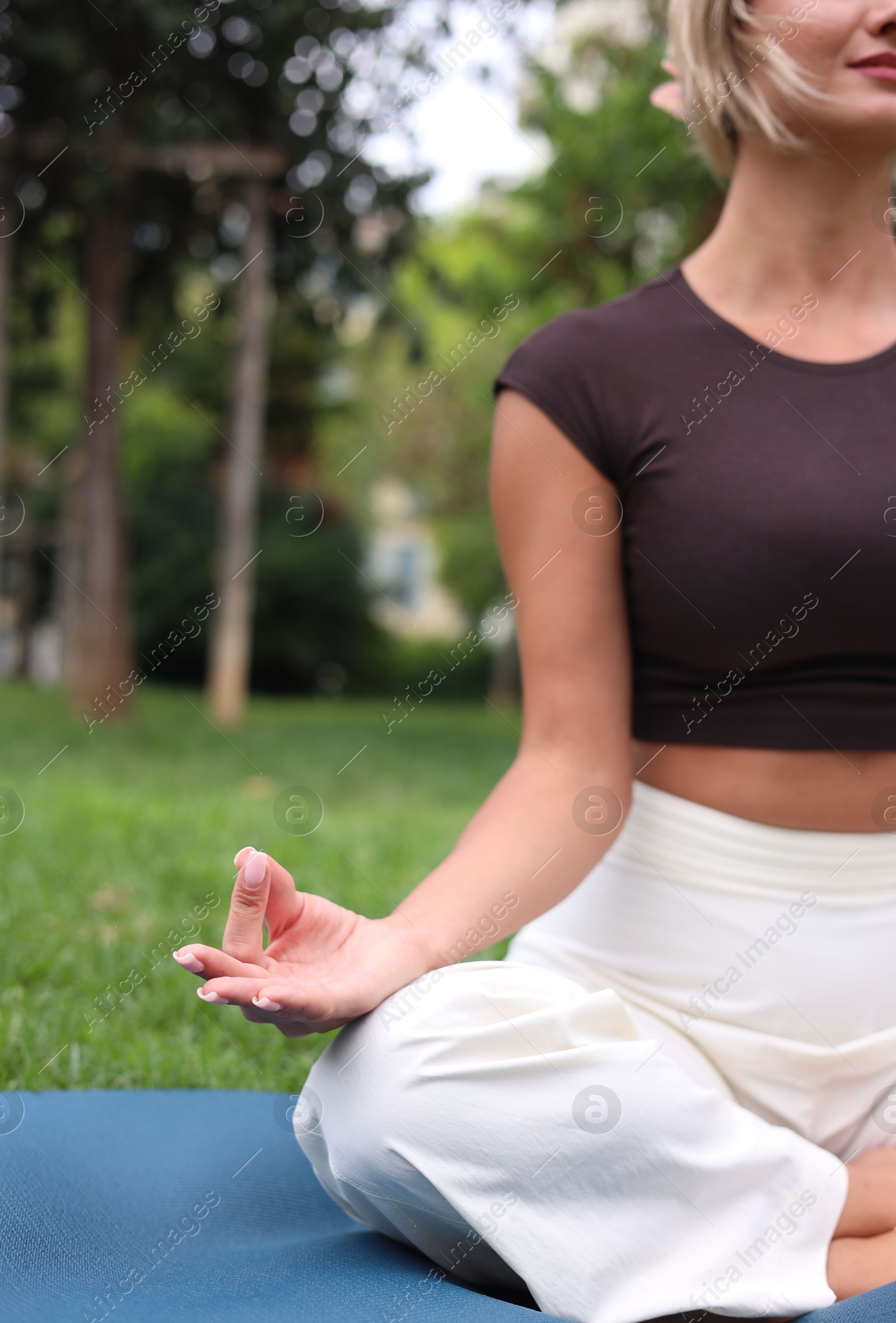 Photo of Young woman practicing yoga on mat in park, closeup