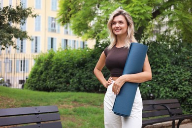 Photo of Beautiful young woman with yoga mat outdoors, space for text