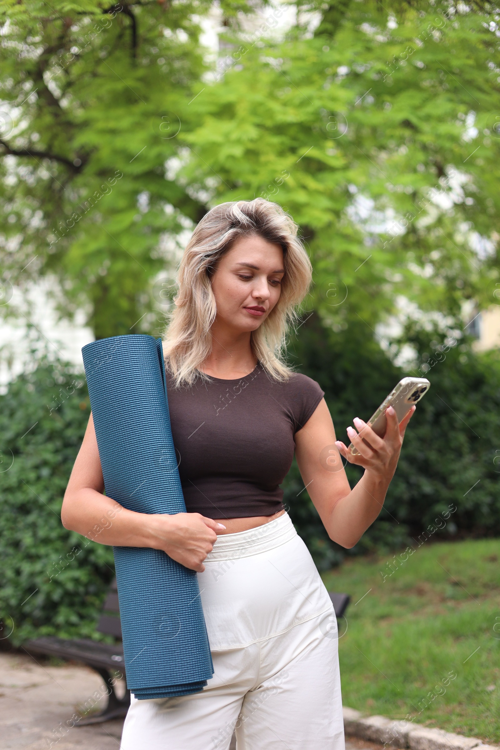 Photo of Beautiful young woman with yoga mat and phone outdoors