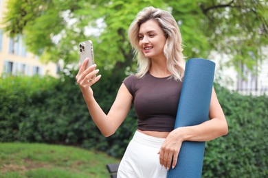 Photo of Beautiful young woman with yoga mat and phone outdoors