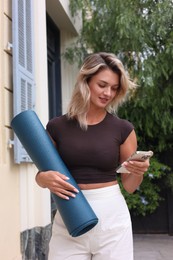 Photo of Beautiful young woman with yoga mat and phone outdoors