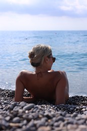 Photo of Woman in bikini lying on pebble beach, back view