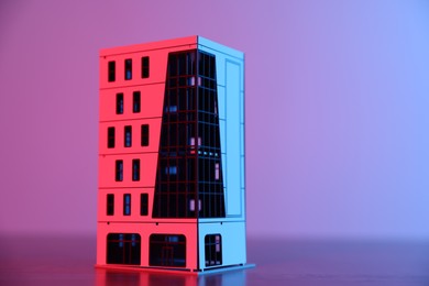 Photo of Real estate. Apartment building model on table in neon lights, closeup. Space for text
