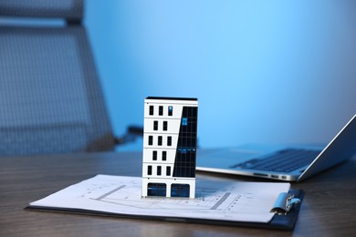Photo of Real estate. Apartment building model, architectural drawings and laptop on table indoors, closeup