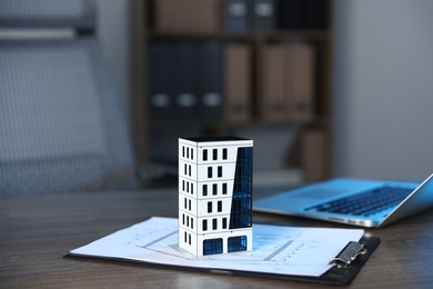 Photo of Real estate. Apartment building model, architectural drawings and laptop on table indoors, closeup