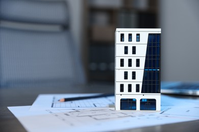 Photo of Real estate. Apartment building model and architectural drawings on table indoors, closeup. Space for text