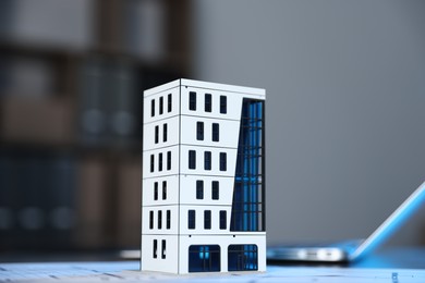 Photo of Real estate. Apartment building model, architectural drawings and laptop on table indoors, closeup