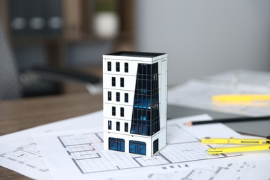 Photo of Real estate. Apartment building model and paperwork on table indoors, closeup