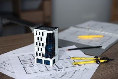 Photo of Real estate. Apartment building model and paperwork on table indoors, closeup