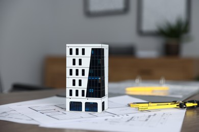 Photo of Real estate. Apartment building model and paperwork on table indoors, closeup