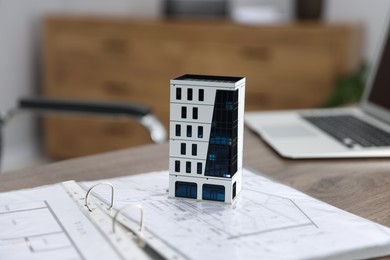 Photo of Real estate. Apartment building model, architectural drawings and laptop on table indoors, closeup