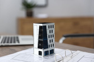 Photo of Real estate. Apartment building model, architectural drawings and laptop on table indoors, closeup
