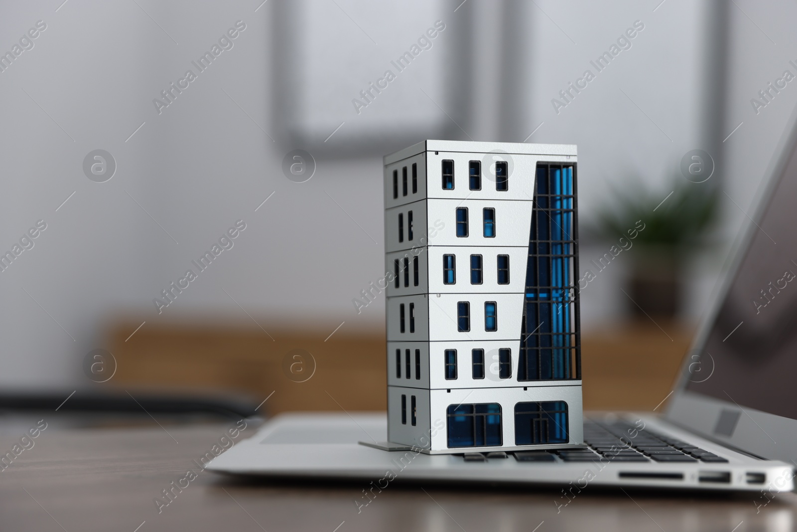 Photo of Real estate. Apartment building model and laptop on table indoors, closeup