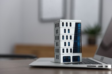 Photo of Real estate. Apartment building model and laptop on table indoors, closeup