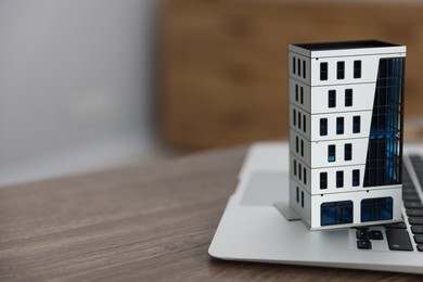 Photo of Real estate. Apartment building model and laptop on table indoors, closeup. Space for text