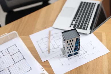 Photo of Real estate. Apartment building model, architectural drawings and laptop on table indoors, closeup