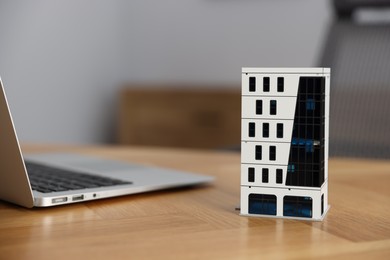 Photo of Real estate. Apartment building model and laptop on table indoors, closeup. Space for text