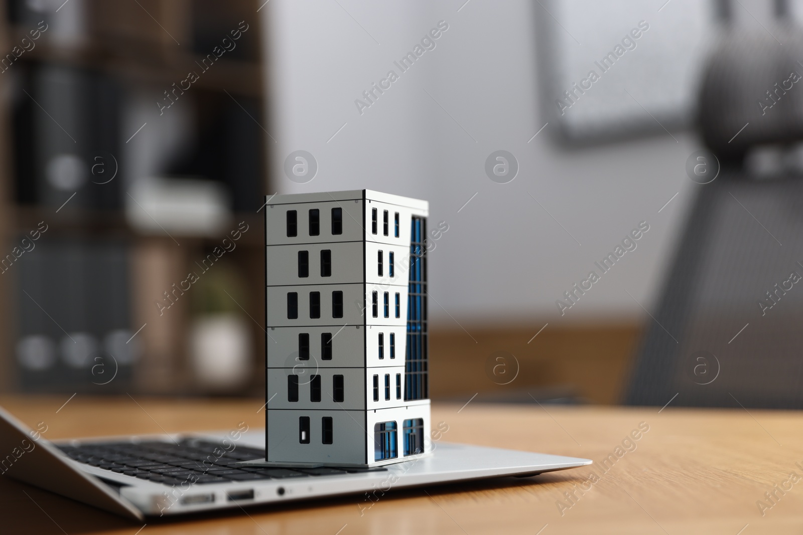 Photo of Real estate. Apartment building model and laptop on table indoors, closeup. Space for text