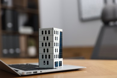 Photo of Real estate. Apartment building model and laptop on table indoors, closeup. Space for text