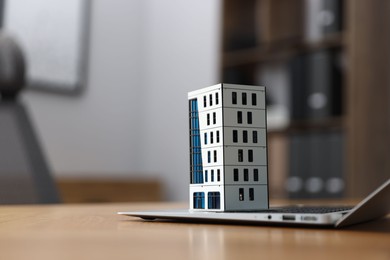 Photo of Real estate. Apartment building model and laptop on table indoors, closeup. Space for text
