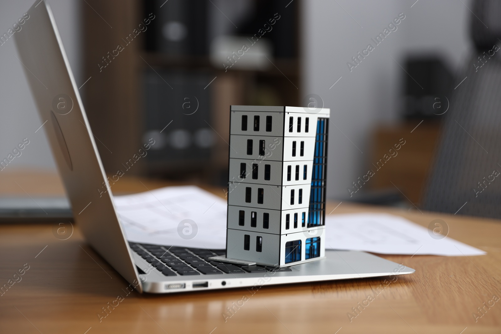 Photo of Real estate. Apartment building model, paperwork and laptop on table indoors, closeup