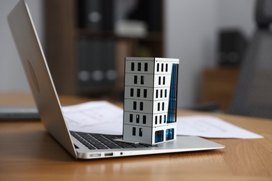 Photo of Real estate. Apartment building model, paperwork and laptop on table indoors, closeup