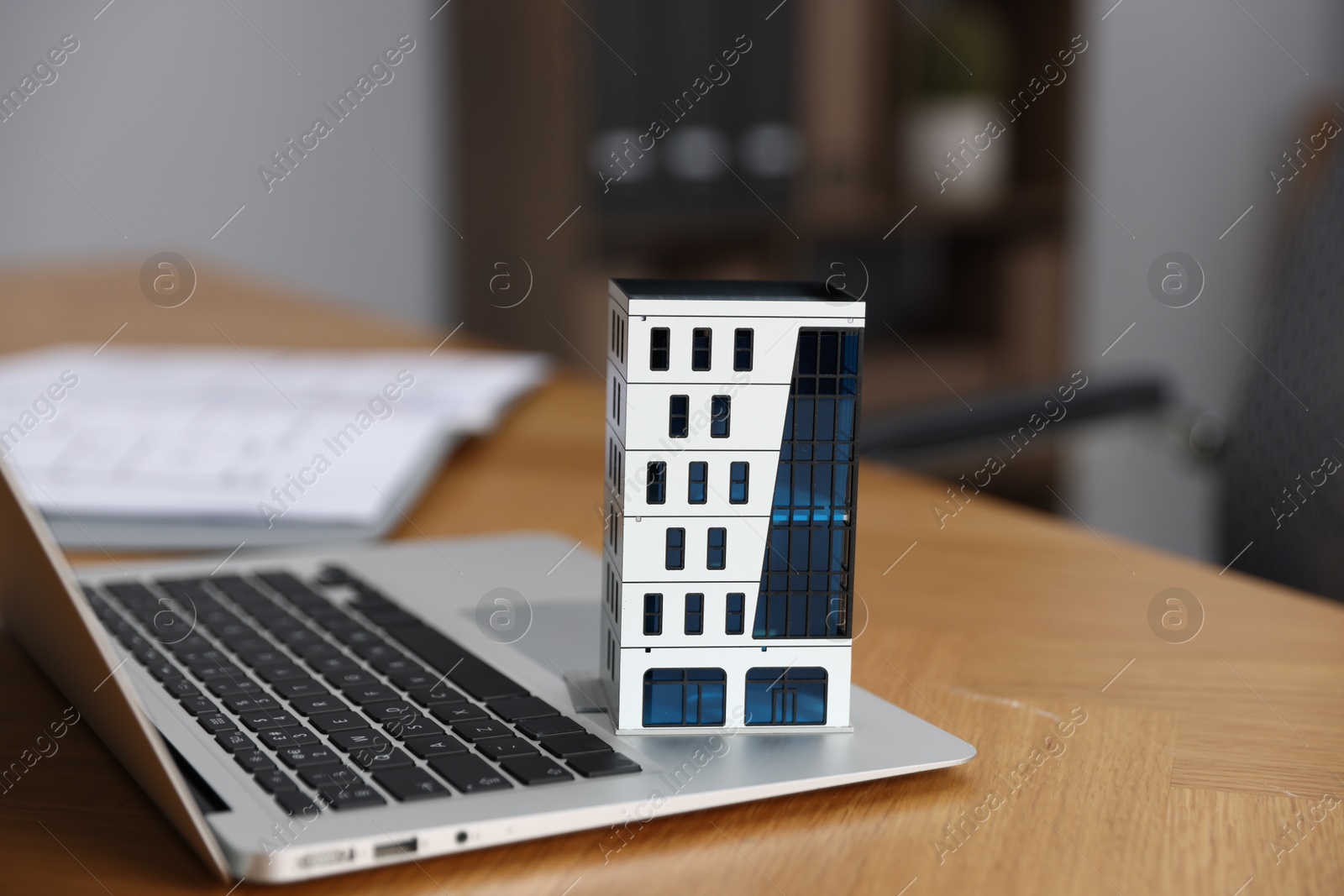 Photo of Real estate. Apartment building model and laptop on table indoors, closeup