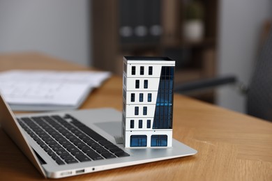 Photo of Real estate. Apartment building model and laptop on table indoors, closeup