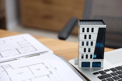 Photo of Real estate. Apartment building model, architectural drawings and laptop on table indoors, closeup. Space for text