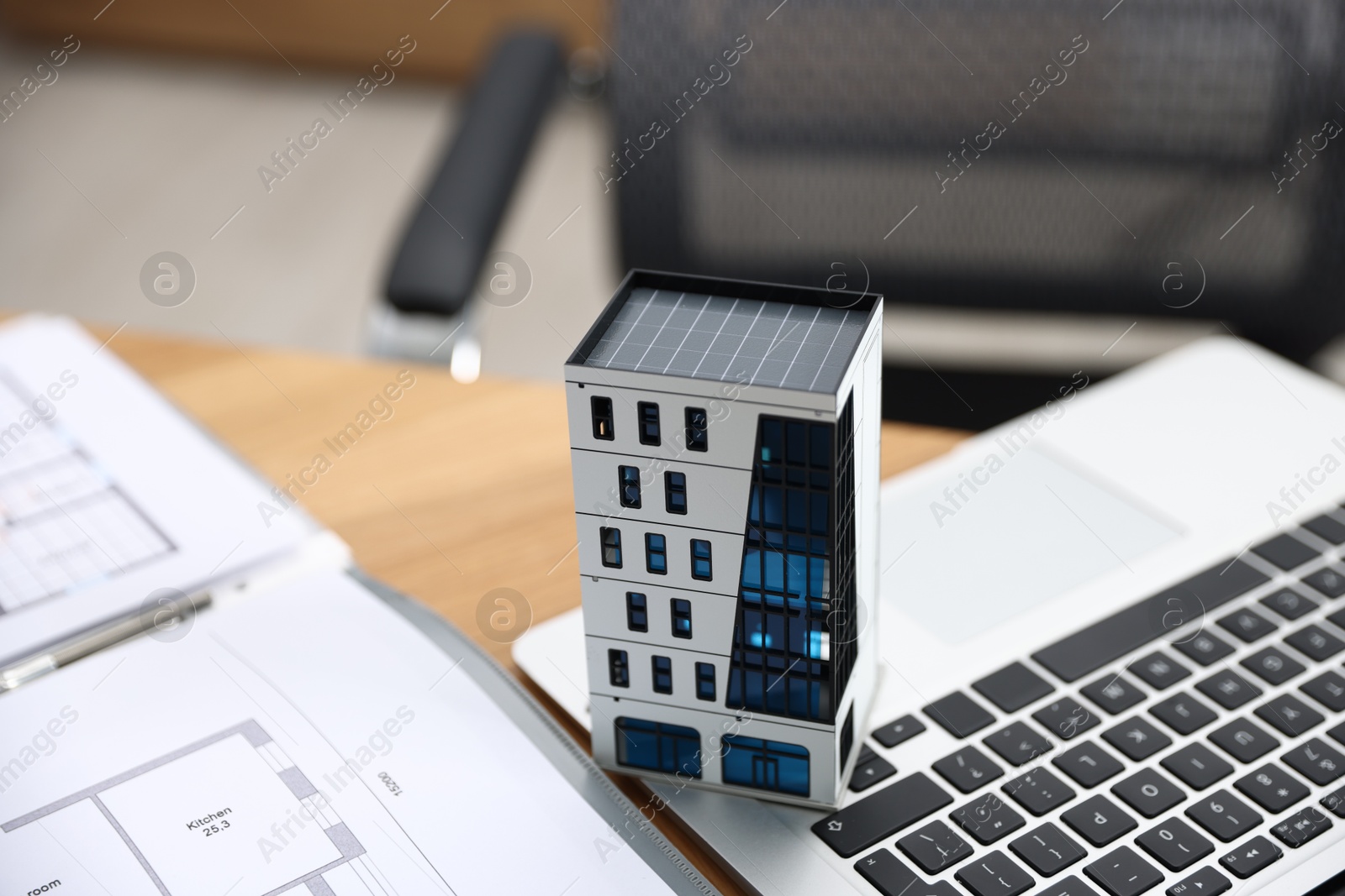 Photo of Real estate. Apartment building model, architectural drawings and laptop on table indoors, closeup