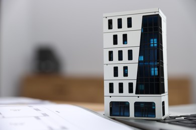 Photo of Real estate. Apartment building model, paperwork and laptop on table indoors, closeup. Space for text
