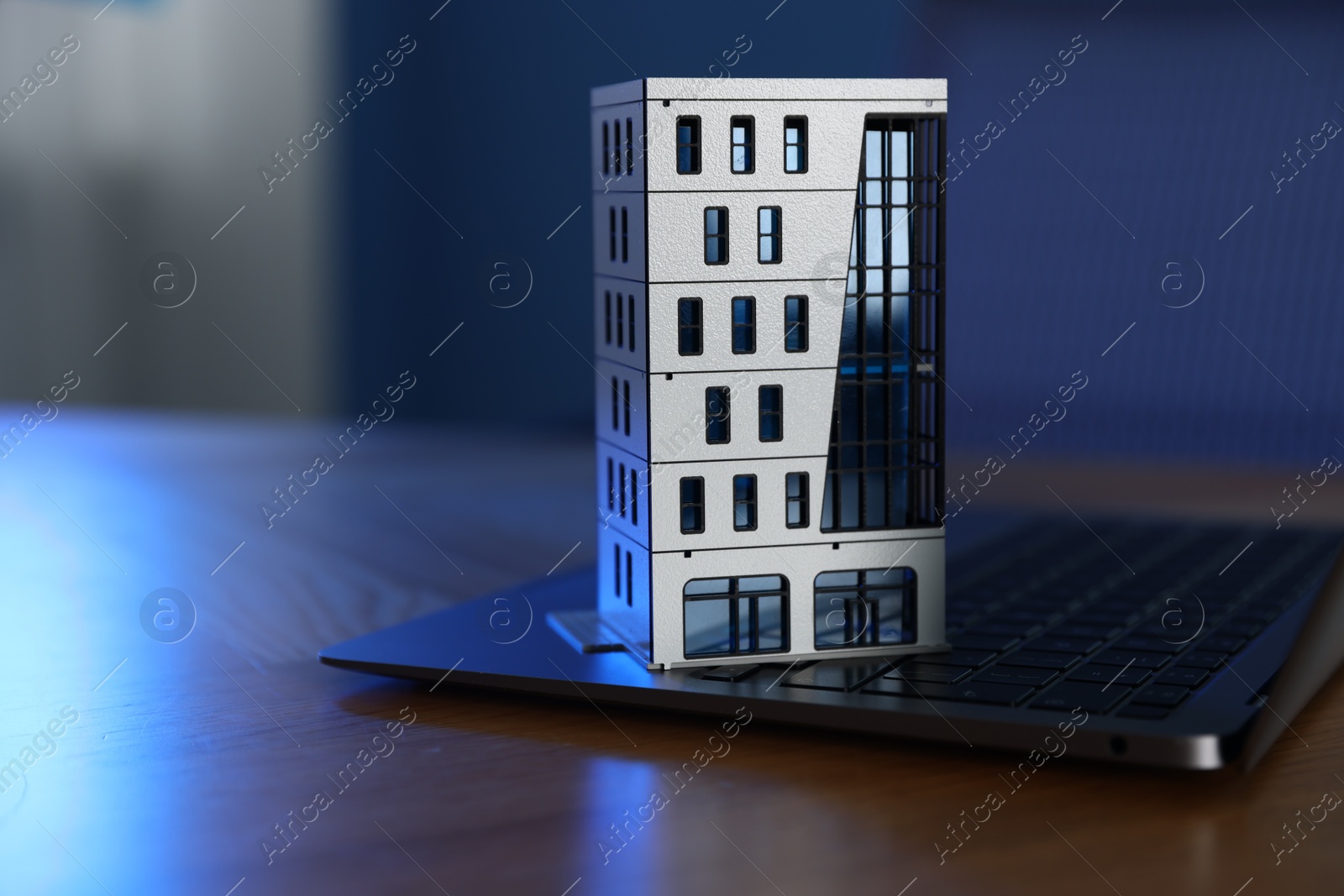 Photo of Real estate. Apartment building model and laptop on table indoors, closeup