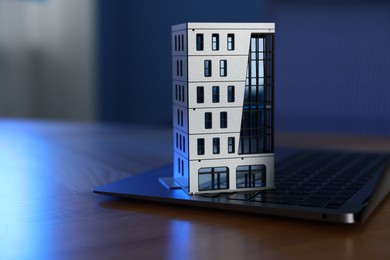 Photo of Real estate. Apartment building model and laptop on table indoors, closeup