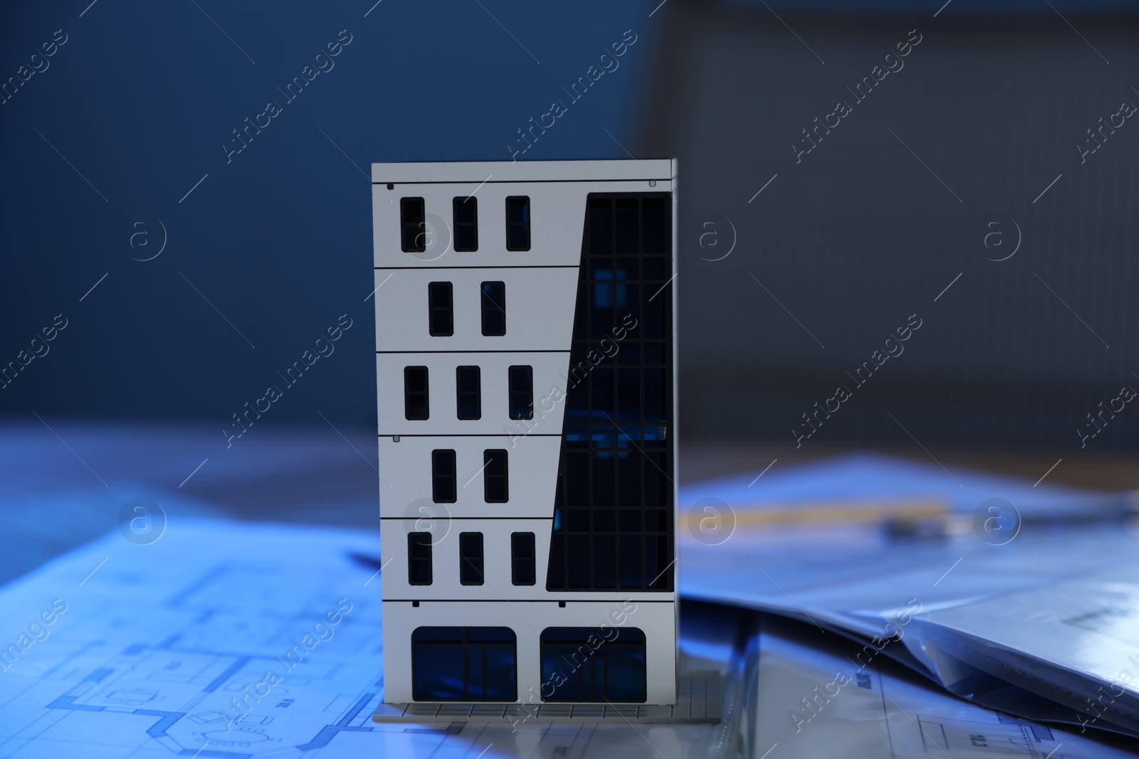 Photo of Real estate. Apartment building model and paperwork on table indoors, closeup
