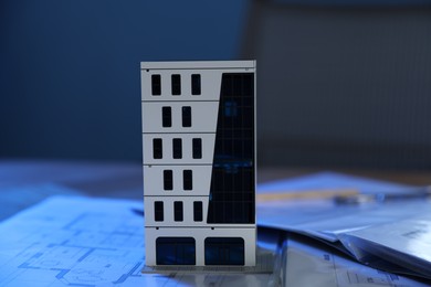 Photo of Real estate. Apartment building model and paperwork on table indoors, closeup