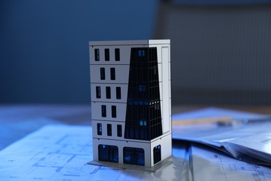 Photo of Real estate. Apartment building model and paperwork on table indoors, closeup