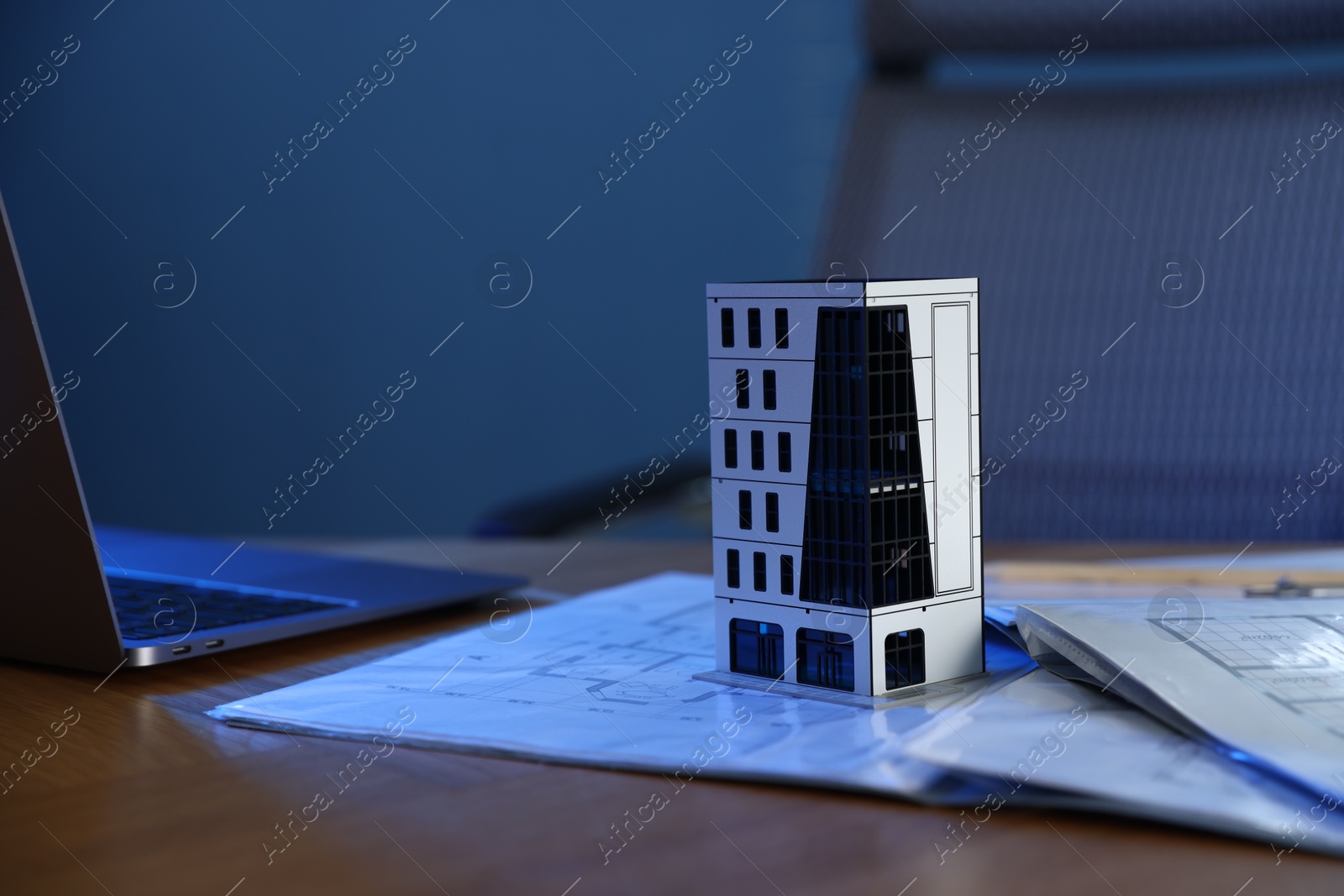 Photo of Real estate. Apartment building model, architectural drawings and laptop on table indoors, closeup